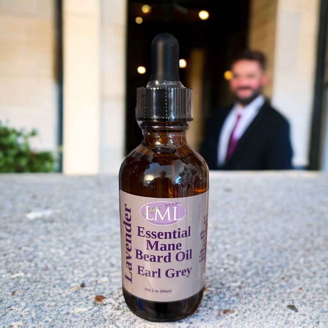 Little Mount Lavender Earl Grey beard oil in an amber glass dropper bottle with a blurred man in a suit background.