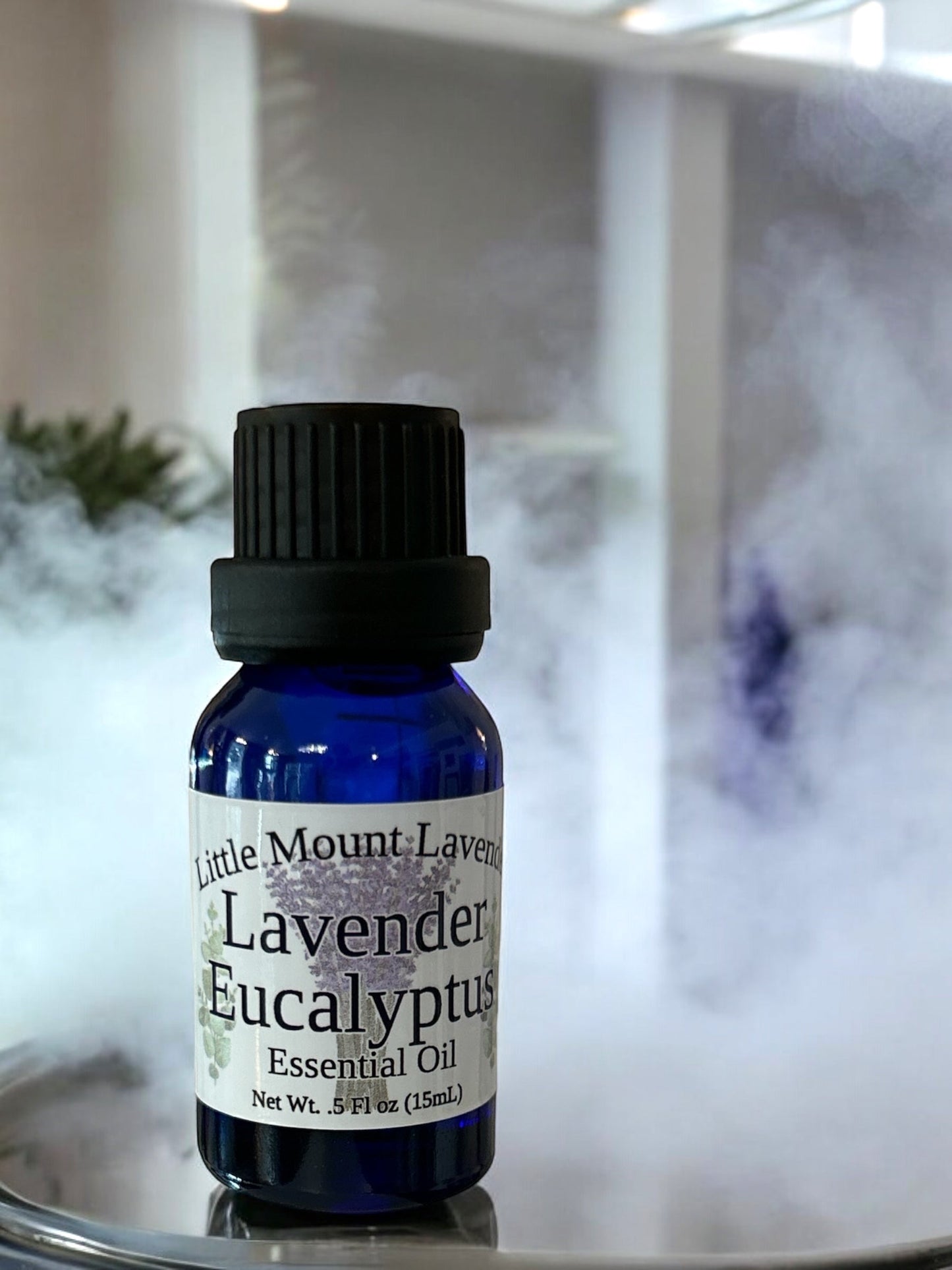 Little Mount Lavender essential oil bottle in blue glass with a black cap, surrounded by aromatic mist for wellness.