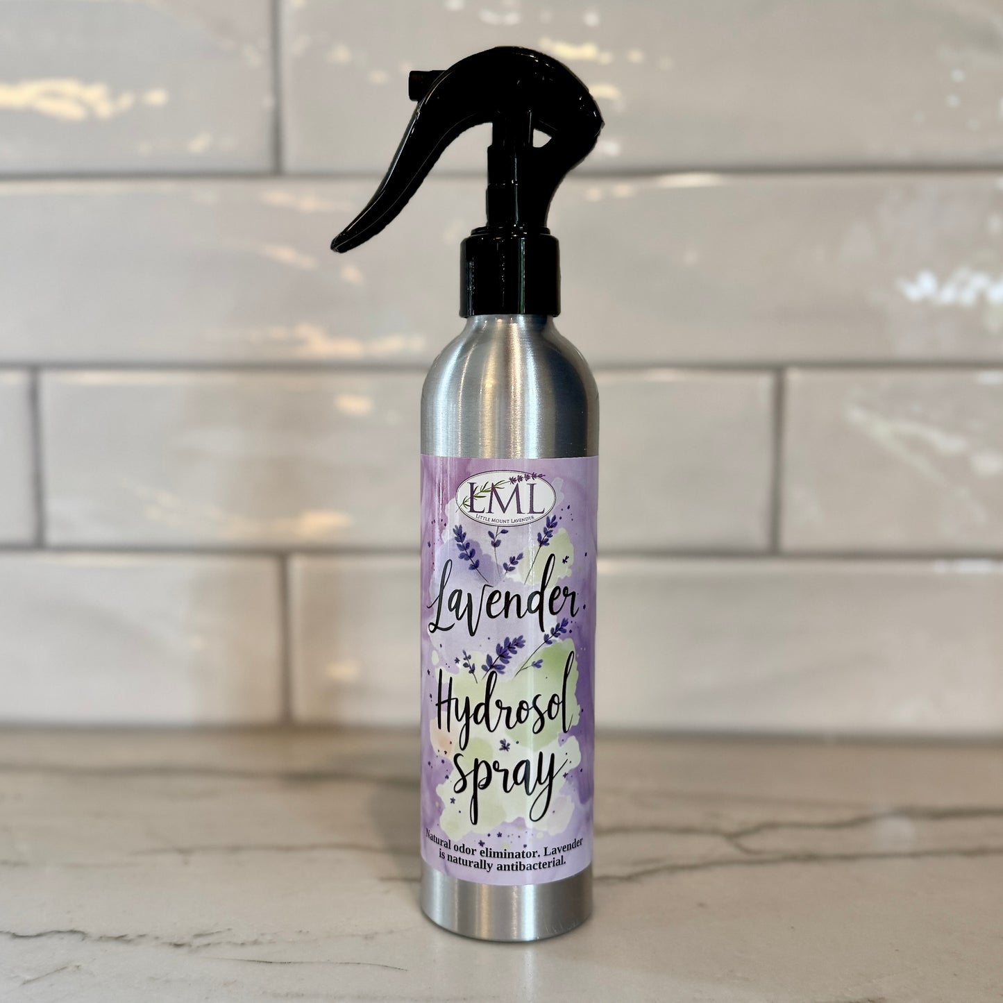 Silver spray bottle with lavender hydrosel label on a tiled wall background