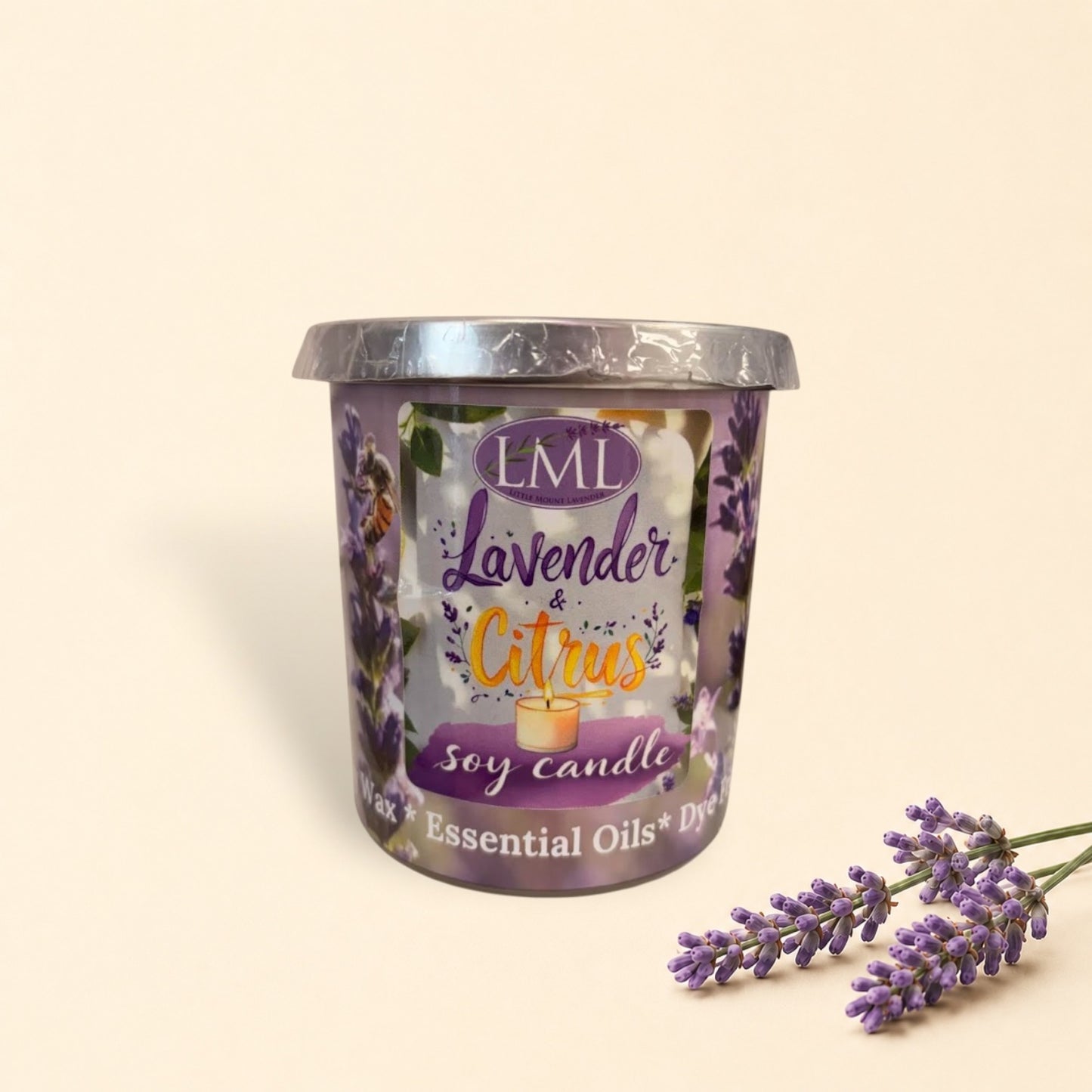 Little Mount Lavender soy candle in a purple glass jar surrounded by fresh oranges and essential oil on a table.
