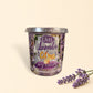 Little Mount Lavender soy candle in a purple glass jar surrounded by fresh oranges and essential oil on a table.