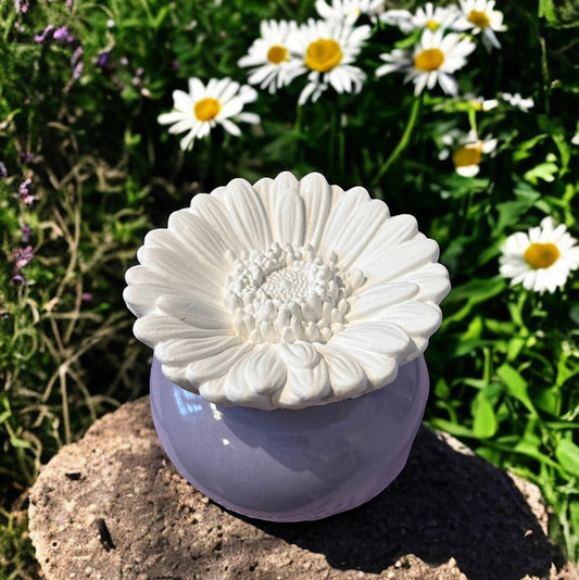 Little Mount Lavender porcelain daisy essential oil diffuser with a light purple base, set outdoors among daisies.