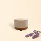 Little Mount Lavender Drum Mist ultrasonic diffuser with wood grain base and white top on a desk with a plant and book.