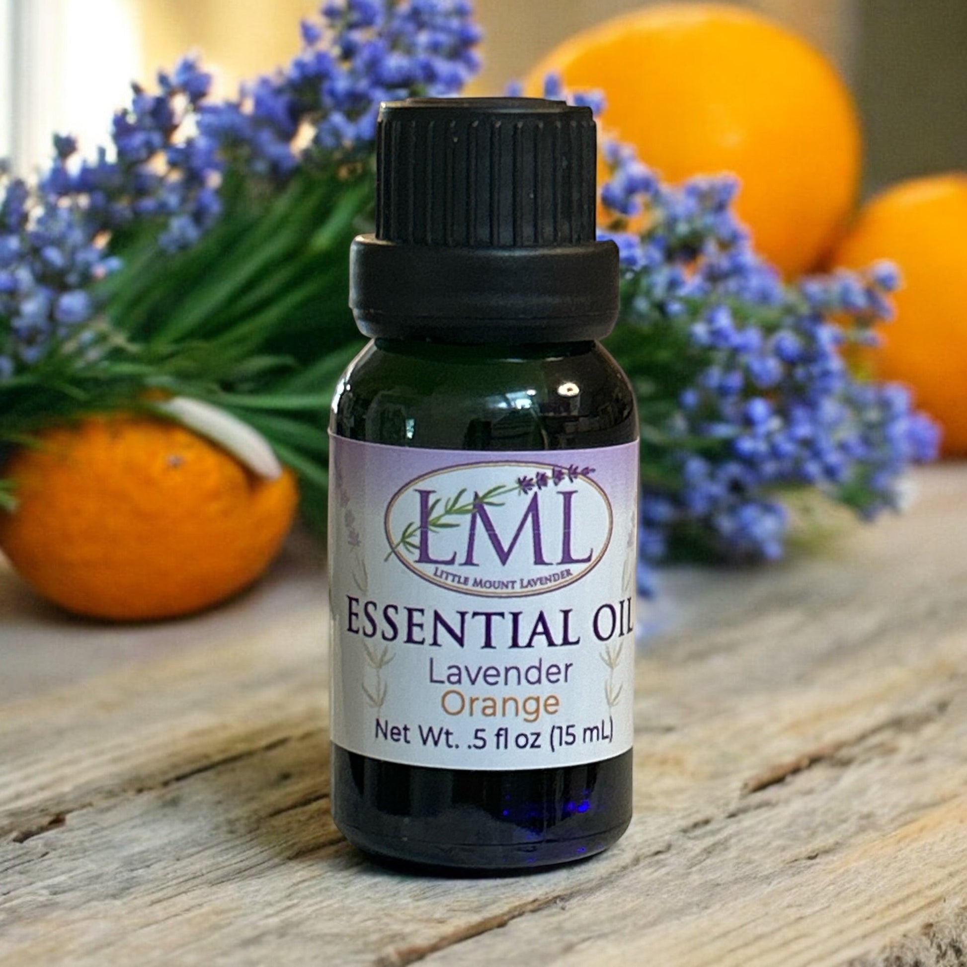 Little Mount Lavender essential oil bottle with lavender sprigs and fresh oranges on a rustic wooden surface.
