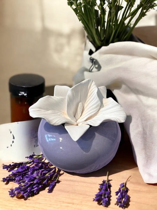 Little Mount Lavender Iris porcelain diffuser with a white ceramic flower on a round lavender base, near dried herbs.