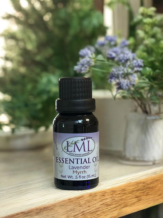 Little Mount Lavender Lavender Myrrh essential oil in a dark glass bottle on a wooden surface with floral background.