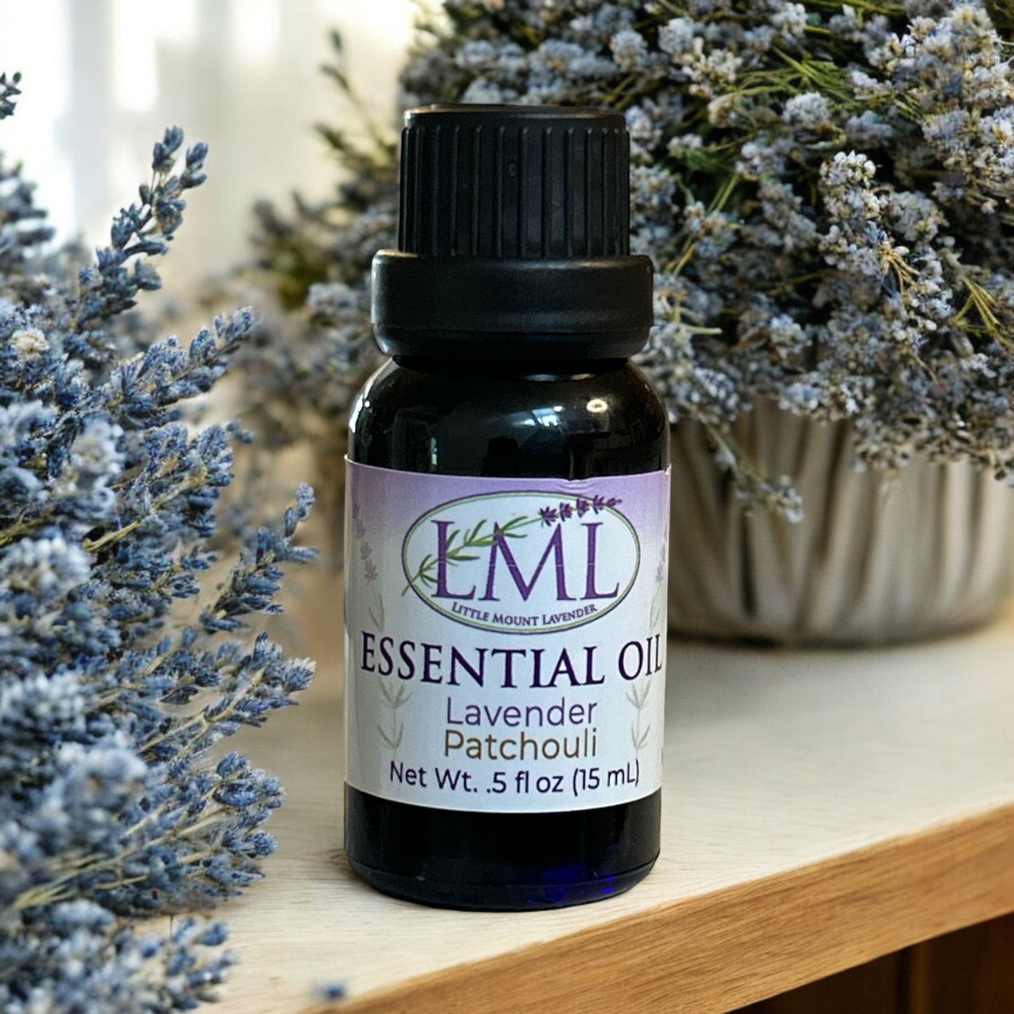 Little Mount Lavender essential oil bottle with lavender and patchouli blend, set against dried lavender flowers.
