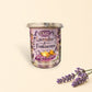 Little Mount Lavender soy candle in a purple glass jar with lavender floral print, surrounded by golden wax melts.