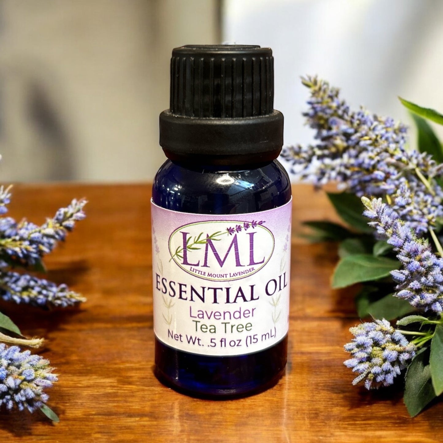 Little Mount Lavender tea tree essential oil in a blue glass bottle surrounded by fresh lavender sprigs.